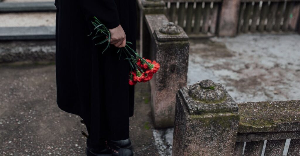 A somber scene of a person holding red flowers near a tombstone at a cemetery.